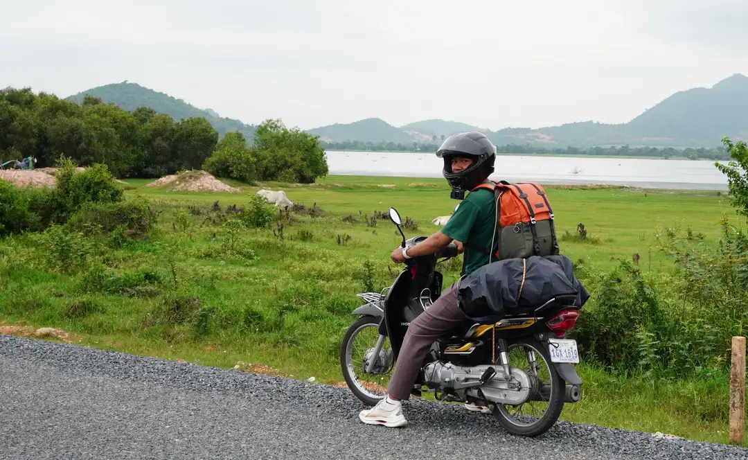 Un voyageur contemple une vallée de montagne au coucher du soleil, sa moto chargée à ses côtés